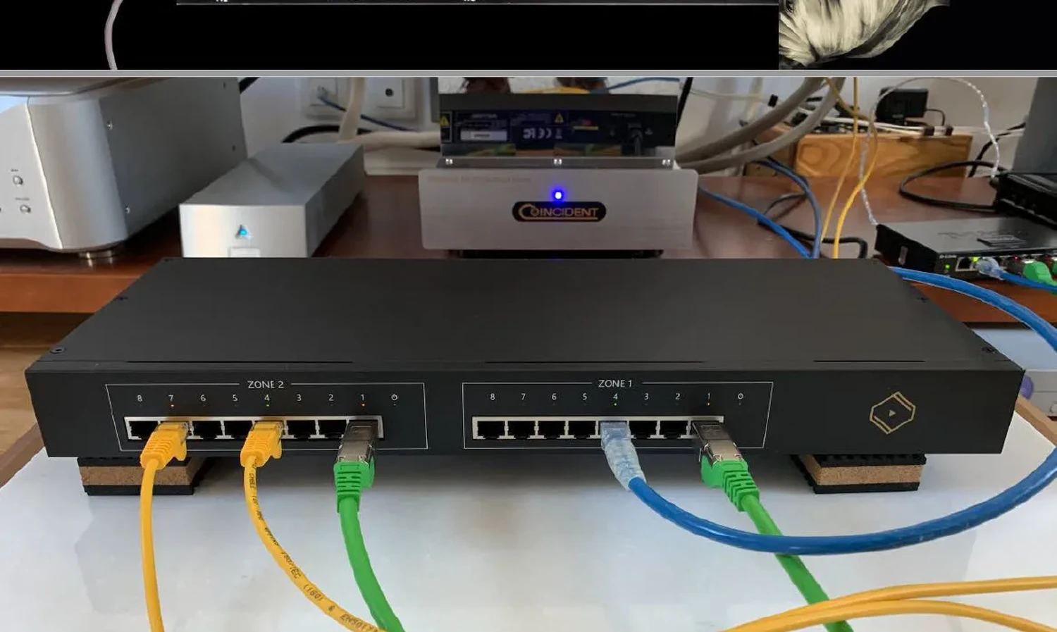 Vue de face d'un commutateur réseau noir Silent Angel N16 LPS avec ses 2 zones, câbles Ethernet de couleur connectés à d'autres appareils Hi-fi en arrière-plan (par 1877.audio)