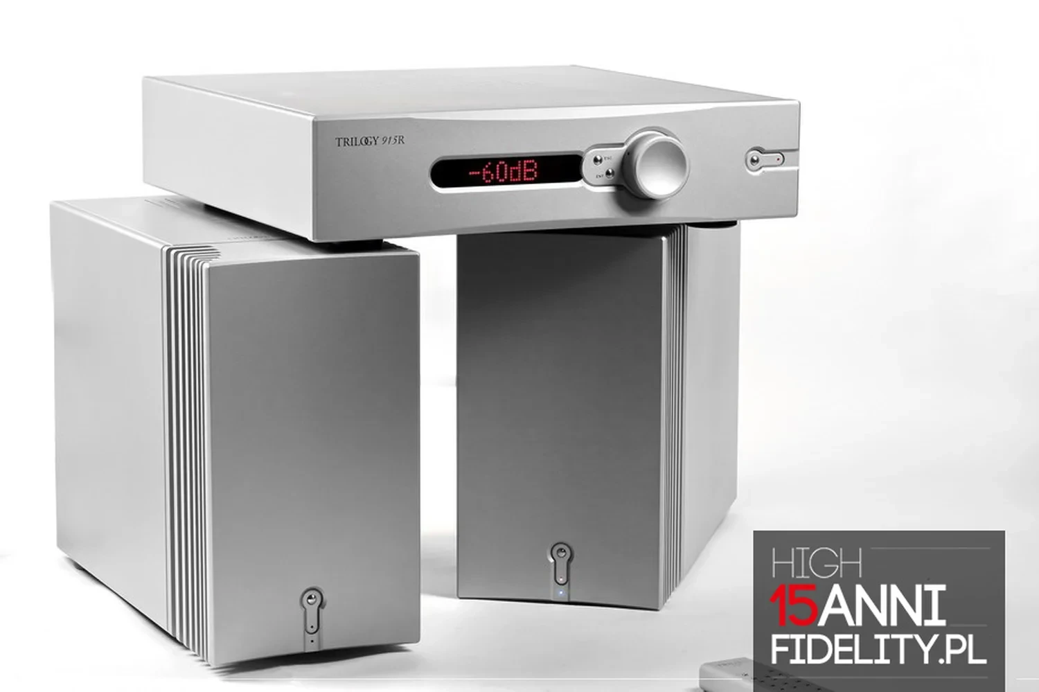 Un amplificateur audio haut de gamme Trilogy Audio 915R doté d'un affichage numérique indiquant -60 dB posé sur deux blocs mono 995R, le tout sur fond blanc avec le logo du journal Fidelity.pl (par 1877.audio)