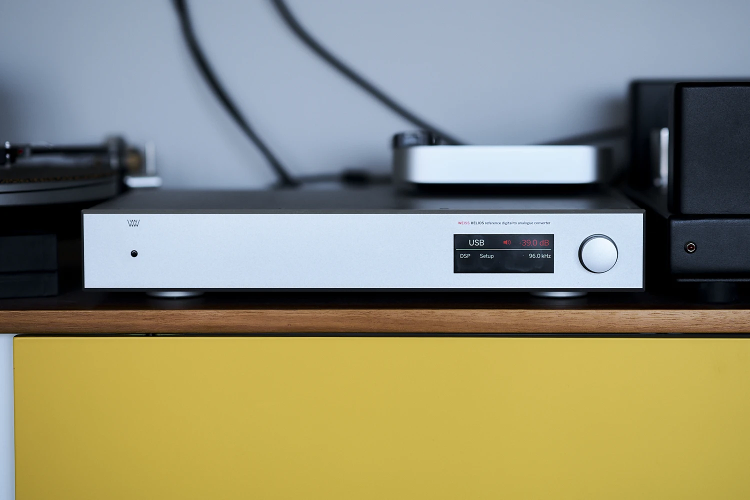 Le DAC Weiss Helios est posé sur une étagère en bois avec d'autres équipements Hi-fi dans une configuration domestique (par 1877.audio)