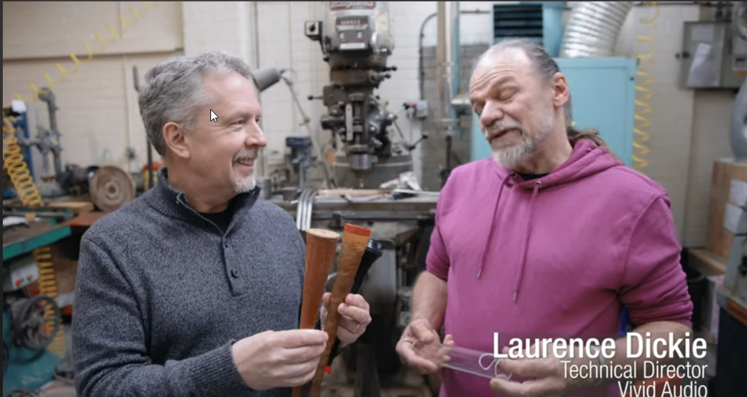 Deux hommes discutant dans un atelier avec des machines en arrière-plan, celui de gauche tient des cônes d'absorption et celui de droite est Laurence Dickie, directeur technique chez Vivid Audio (par 1877.audio)