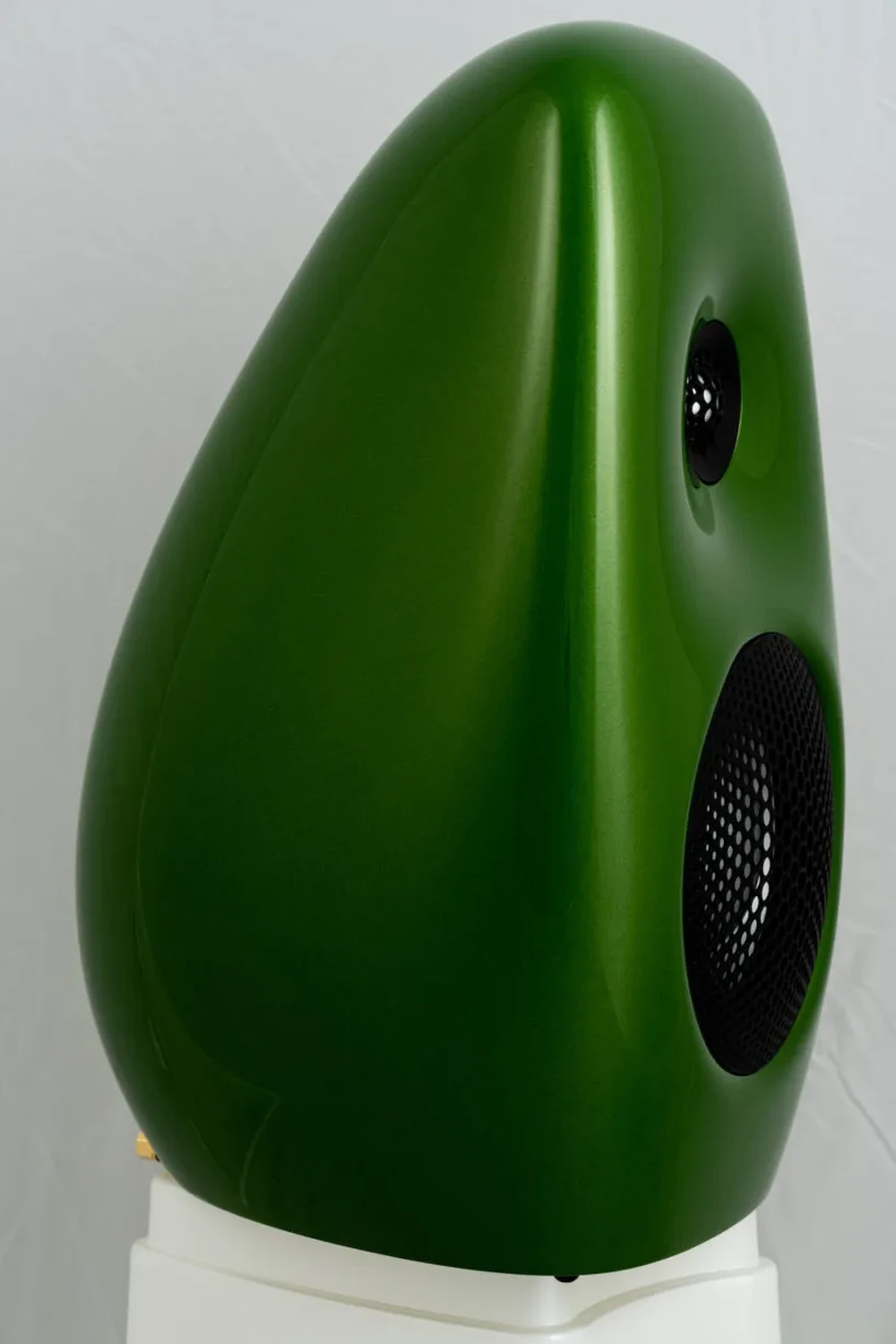 Une enceinte Vivid Audio Kaya S12 verte en forme de poire avec grilles de haut-parleurs à l'avant, posée sur un pied blanc en plastique (par 1877.audio)