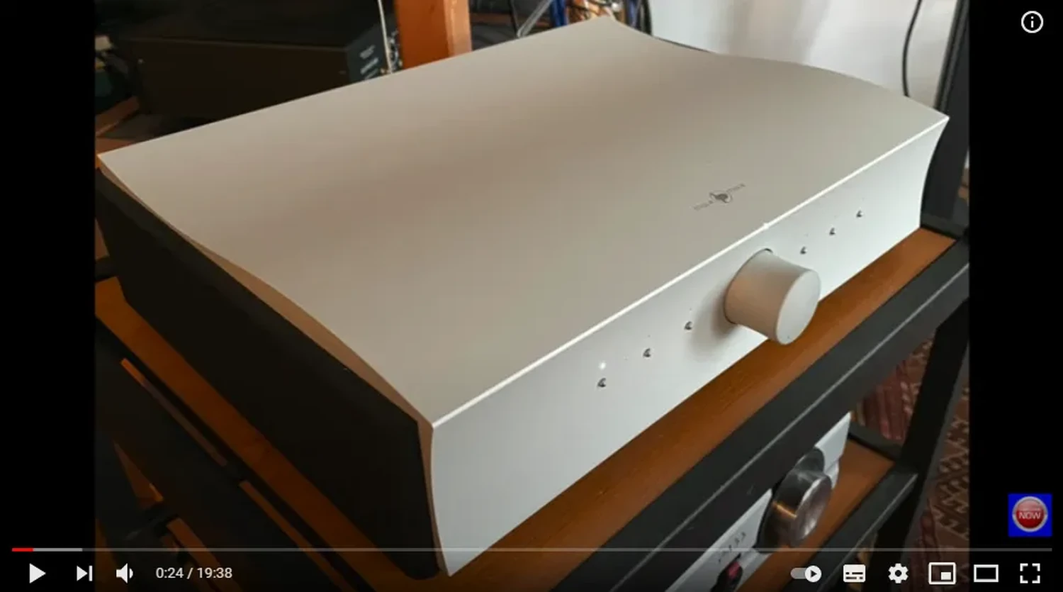 Un amplificateur intégré Mola-Mola Kula avec son un boîtier aluminium avec un grand bouton de volume, 6 boutons avec leur LED blanche respective sur un rack audiophile en bois (par 1877.audio)